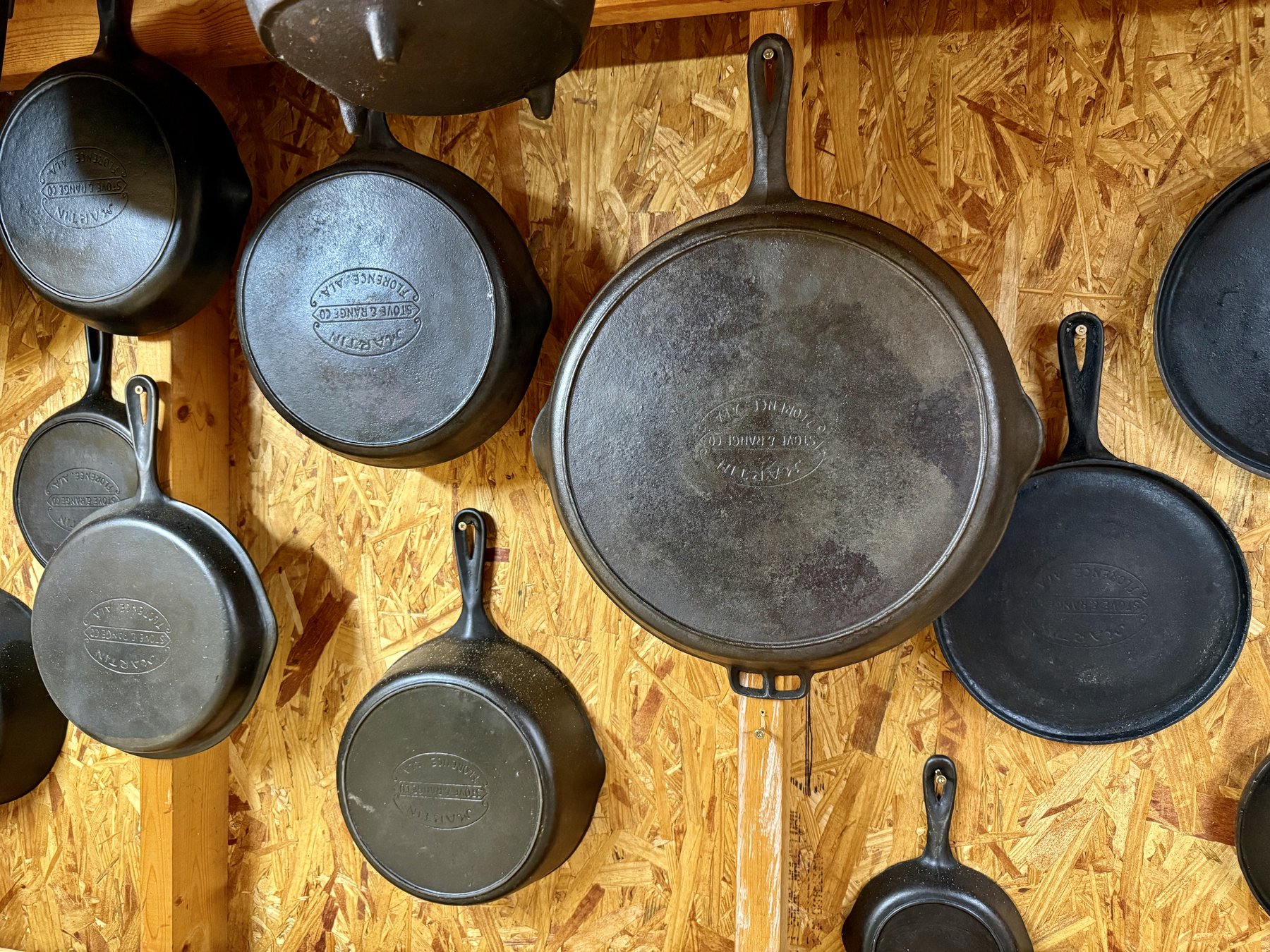 Wall of Martin Stove & Range hamburger-logo cast iron — skillets, griddles, and a deep pan with lid, Florence Alabama marks showing